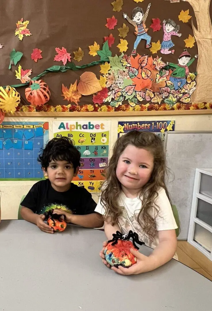 Children holding decorated pumpkins in classroom.